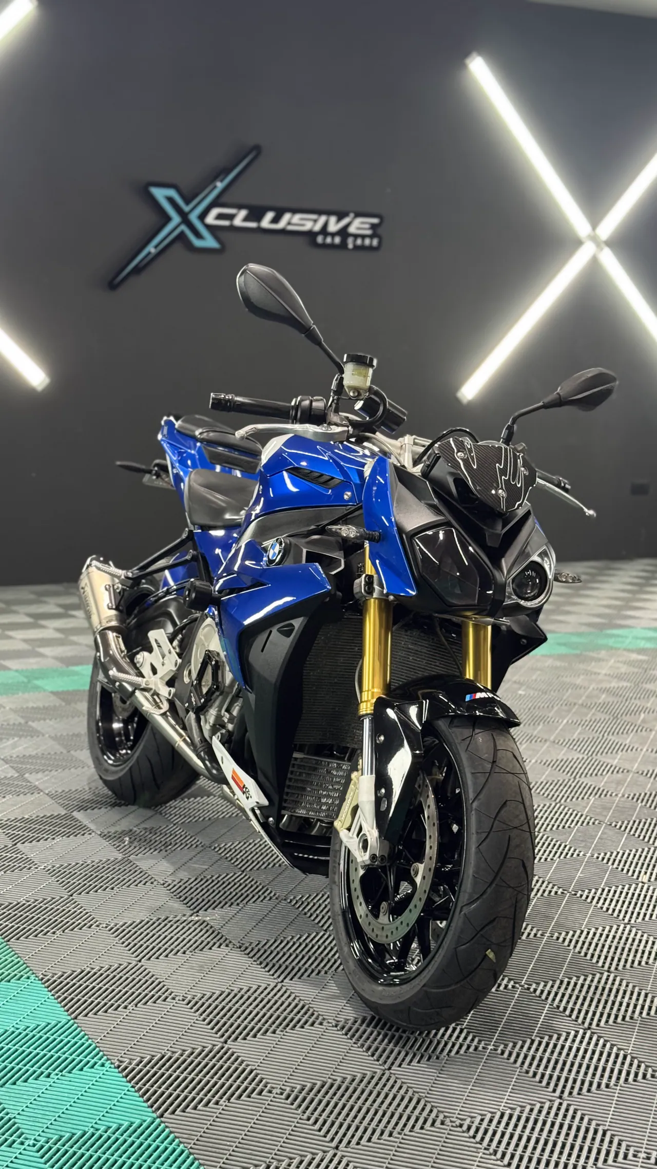 Motocicleta naked azul frente al logo de Xclusive